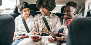 Three young people smiling as they use the Zelle App in the backseat of a car